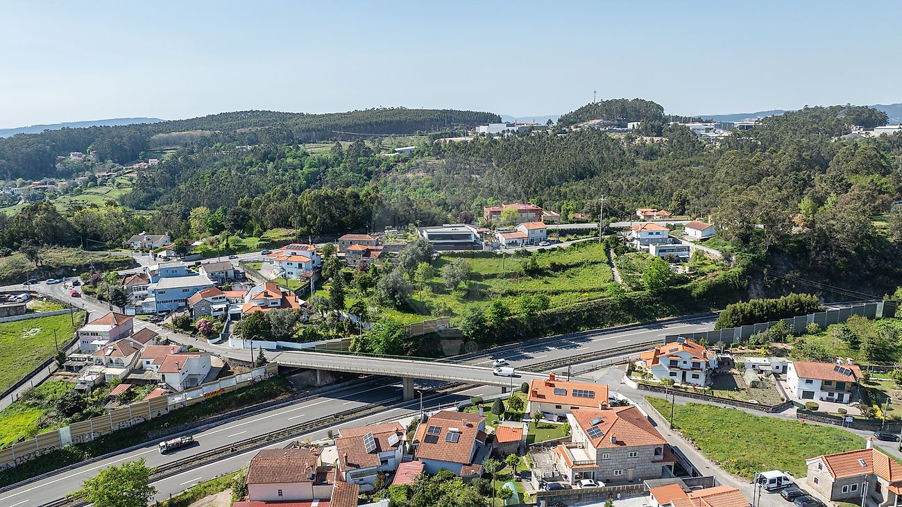 Fotografia aérea ampla de drone em plano geral realçando a envolvência natural, encostas e a malha urbana onde se insere o lote de terreno