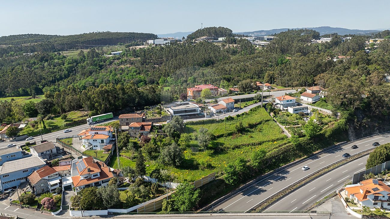 Vista de drone lateral focada na morfologia do terreno, moradias vizinhas com painéis solares e conectividade com a rede de estradas de Famalicão