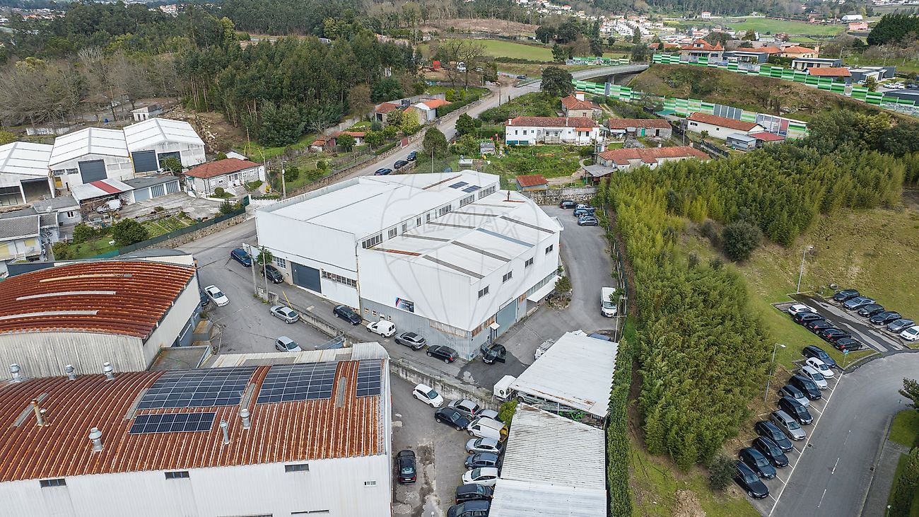 Perspetiva aérea lateral do pavilhão industrial em Famalicão evidenciando os acessos pavimentados e parqueamento de viaturas