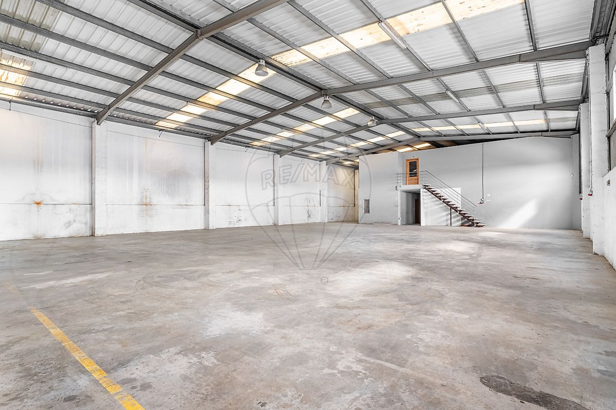 Interior do pavilhão industrial focado na estrutura de pilares e portão de descarga para veículos pesados e camiões